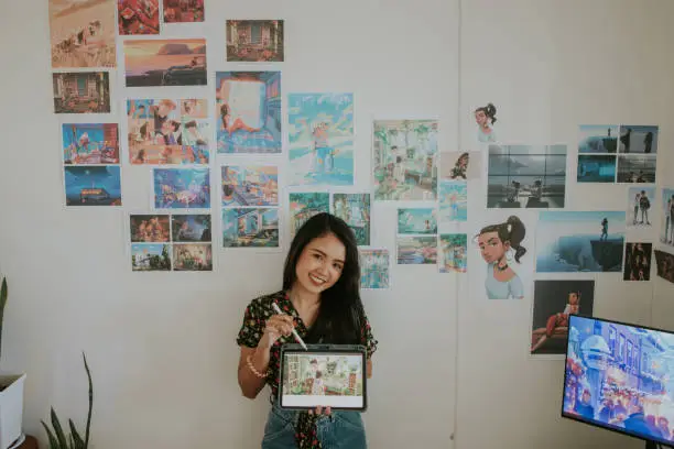 The confident Thai cartoonist designer is proudly presenting her unique portfolio while showing her drawing in the tablet at her own home office, Bangkok Thailand