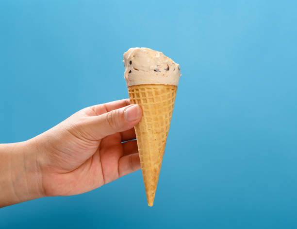 istock hand holding a milk tea flavor ice cream cone with some bites on a blue background horizontal composition 1270736820