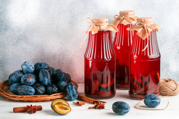 homemade plum compote with cinnamon and star anise. delicious healthy vitamin drink. jars and fresh berries on a light wooden table. home preparations. selective focus, copy space - plum fruit organic food and drink imagens e fotografias de stock