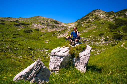 Side view of Senior woman enjoying the shadow, while resting, during hiking near Komna in Triglav national park,  Slovenia. It is hiking destination with mountain cabin near by.