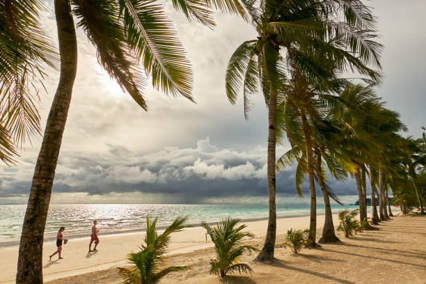 Young couple walking along the clean White Beach Young couple walking along the clean White Beach with coconut trees at sunset with cloudy sky at Boracay Island, Aklan Province, Visayas, Philippines malay couple full body stock pictures, royalty-free photos & images