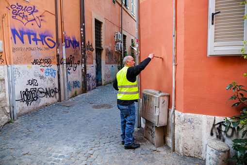 Rome, Italy, February 06 -- A senior man paints the walls of an ancient building in Trastevere to erase vandalism and graffiti, in the heart of Rome, in an area much loved and frequented by residents and tourists, but also very scarred by vandalism. Image in High Definition format.