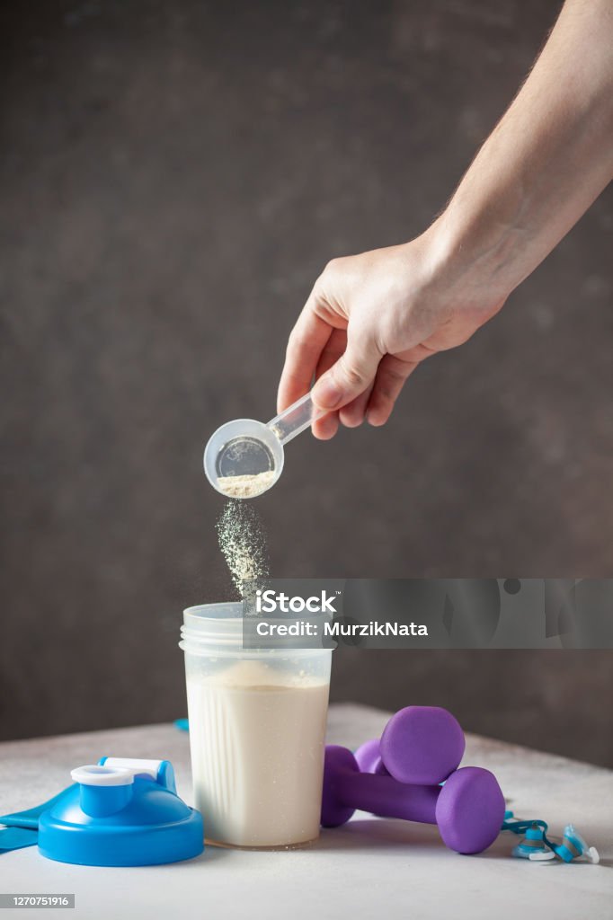 Set of different sauces Protein shake in bottle, powder,  and measuring tape on grey background. Hand fills protein powder into bottle. Sport food concept. Protein Drink Stock Photo