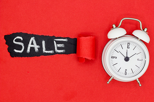 top view of the word sale written on black chalkboard and white alarm clock on red torn paper background