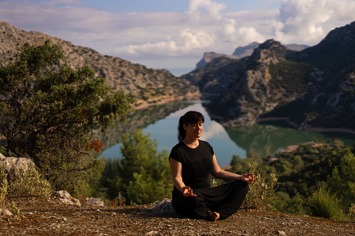 Mature woman practising mindfulness in Majorca's landscape with the reservoir in the background