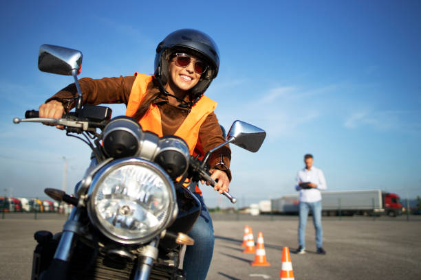 istock Female student with helmet taking motorcycle lessons and practicing ride. In background traffic cones and instructor with checklist rating and evaluating the ride. Motorcycle school of driving. 1270760859