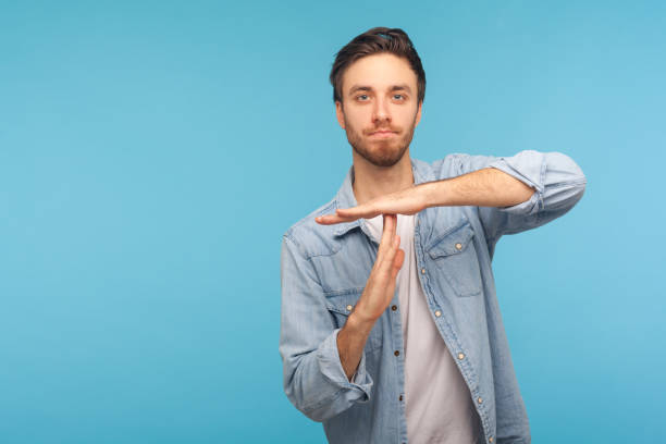 Please, need pause! Portrait of man in worker denim shirt showing time out, refusing and doing enough limit gesture Please, need pause! Portrait of man in worker denim shirt showing time out, refusing and doing enough limit gesture, asking to stop, warning of deadline. studio shot isolated on blue background push pause stock pictures, royalty-free photos & images