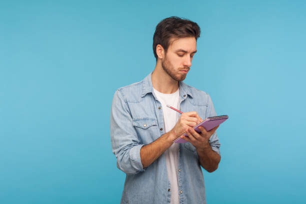 portrait of man journalist in denim shirt making notes in paper notebook, writing business idea, future plans - isolated holding letter people imagens e fotografias de stock