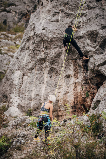 istock Man climbing on rocks while woman is assisting him by holding the rope 1270765572