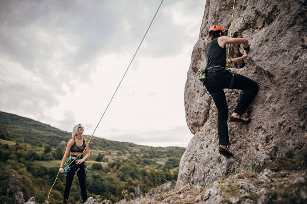 istock Man climbing on rocks while woman is assisting him by holding the rope 1270765728