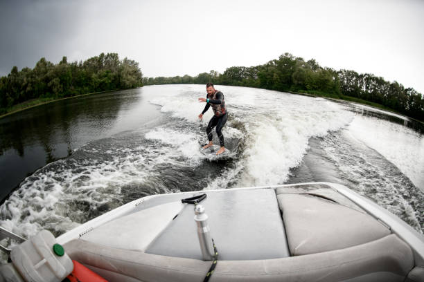 istock Young man rides surfboard on the waves behind boat. 1270767524