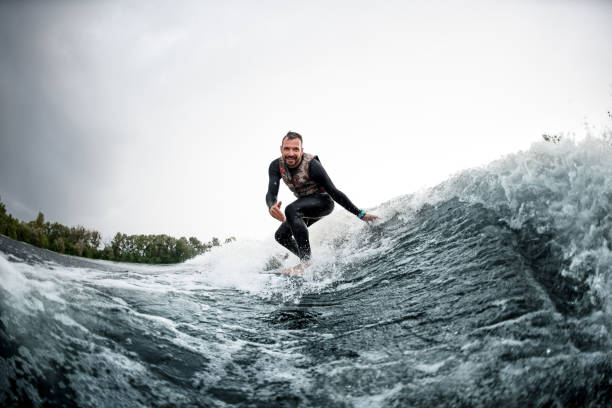 istock Cheerful man rides on surfboard down wave and touches the water 1270770968