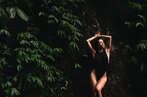 Beautiful young woman relaxing under waterfall in Bali