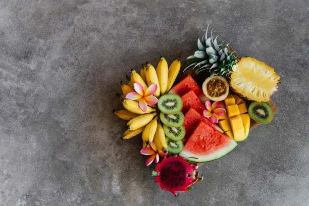 istock Tropical fruits assortment on a wooden plate. Stone background. 1270773003