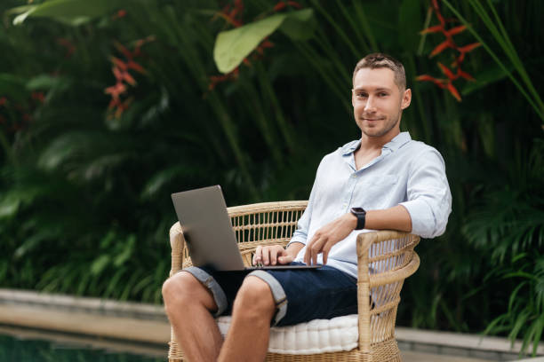 istock Young man using a laptop computer in a garden with a swimming pool. 1270773005