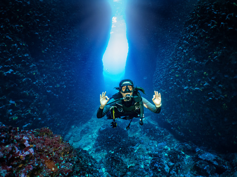 A happy female scuba diver shows the OK sign in front of an underwater cave