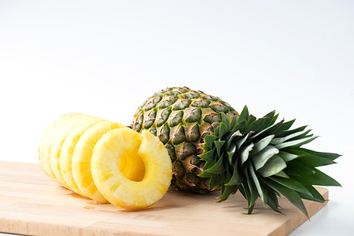 Whole pineapple with pineapple slices on cutting board on white background.