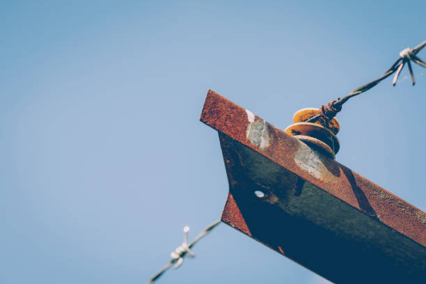 Strand of barbed wire on a spacer or isolator on top of a rusted steel bar or girder against a blue sky