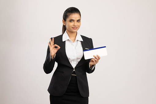 Confident businesswomen holding card and looking at camera while standing against white background