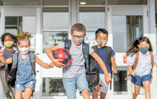 Diverse group of elementary school kids go back to school wearing masks Group of kids return to school during the pandemic. schoolyard stock pictures, royalty-free photos & images