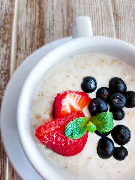 Healthy breakfast. Oatmeal with sliced fresh and ripe strawberries and blueberries in a white bowl on a wooden table.