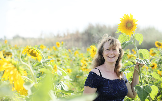Portrait of happy mature woman  enjoying of freedom in the sunflowers field