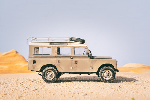 Beaconsfield, UK - September 5, 2020: Scale model of a Series III long wheel-base Land Rover, seen here sitting a dusty desert location, with a clear blue sky overhead. The car is very dirty, suggesting it's been on an extended journey.