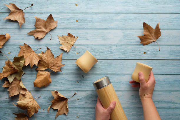 istock Zero waste eco friendly insulated metal flask with bamboo cups. Trendy flat lay with hands holding the flask and cup on aged blue mint wooden background covered with Autumn sycamore leaves. 1270802497