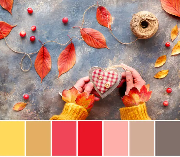 Color matching palette from image of woman hands holding wooden heart. Color palette includes honey dijon shade. Top view of table with Fall handmade decorations from natural materials.