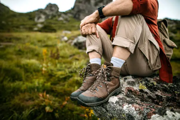 Active Senior Hiker taking a rest after climbing on tall mountain rock