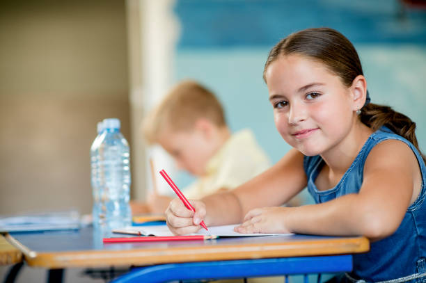 istock Cute schoolgirl smiles at the camera in classroom 1270810375