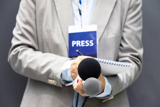 istock Female reporter at press conference or media event, writing notes, holding microphone 1270811612