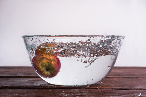 Unusual angle for shooting food. Wet fresh apple. The apple falls into a bowl of water and the sprays fly in different directions.