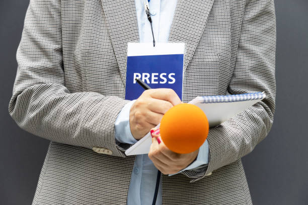istock Journalist at news conference or media event, writing notes, holding microphone 1270819320