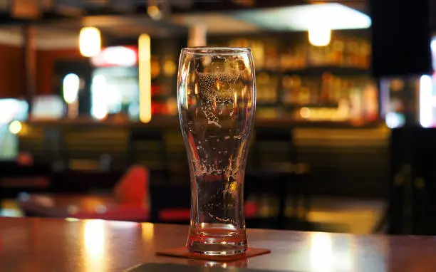 Photo of Empty beer glass on the table in a dark evening bar, panoramic view