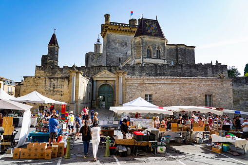 France. Gard (30) The city of Uzes. Medieval City. People walking in a market in front of the Ducal castle known as the Duchy of Uzes and his the Bermonde Tower
