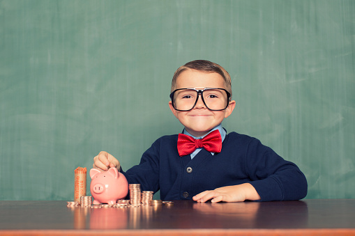 A young boy dressed as a nerd is happy because he is learning to save money for his future retirement in his piggy bank.