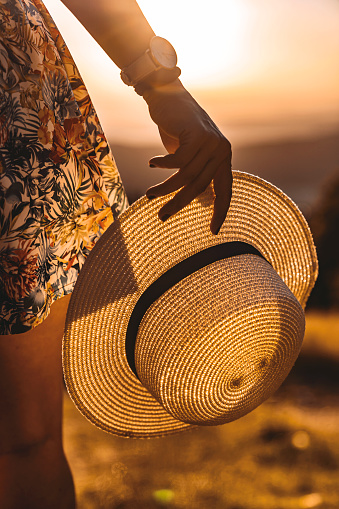 Close up of a straw hat in woman hands with nature sunset in background.
