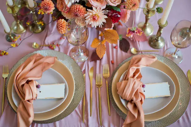 Beautiful table setting with autumn flowers, orange and pink napkins and burning candles. Autumn wedding concept