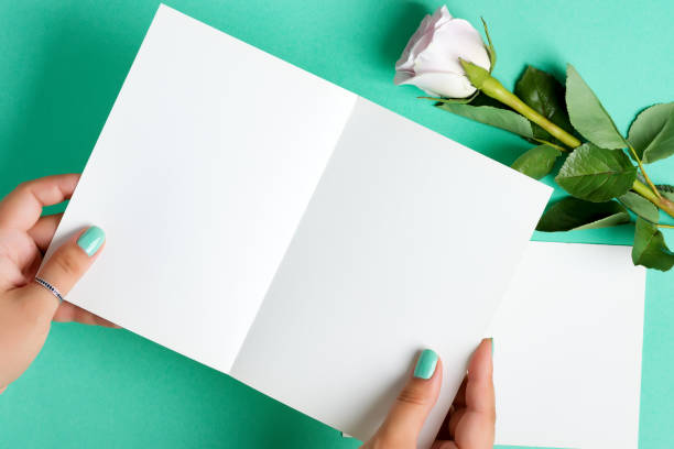 istock Woman's hands are holding empty mock-up paper sheet for writing letter above pastel turquoise background with rose flower. 1270840377