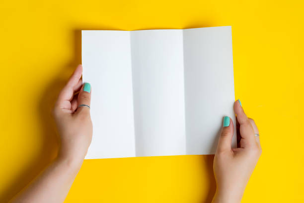 istock Woman's hands are holding empty trifold mock-up brochure for writing letter above yellow background 1270840437