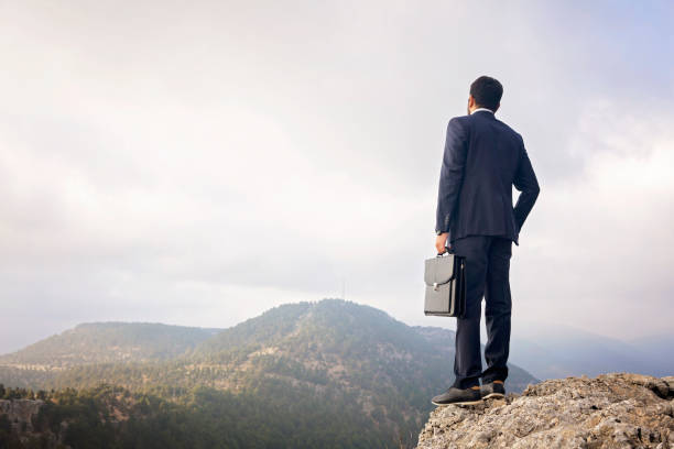 istock Young businessman on top mountain peak over clouds. 1270843403