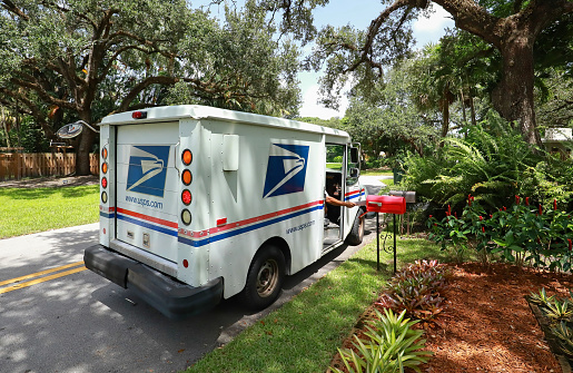 Fort Lauderdale, Florida, USA - September 3, 2020:  Mailman delivering mail in a postal truck puts letters into a red mailbox.