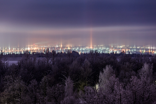 night winter cityscape with light pillars atmospheric phenomenon.