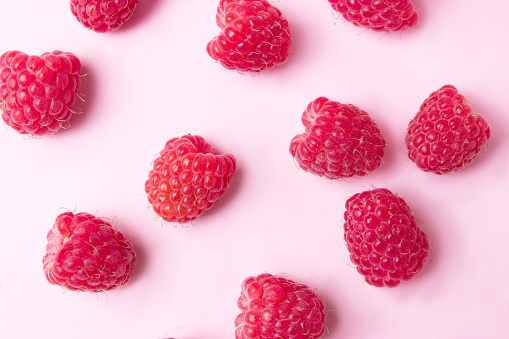 Raspberry on pink background. Flat lay summer berries - red raspberries and mint leaf. Creative minimalism