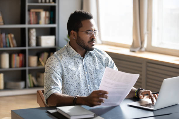 istock Serious confident African American man using laptop, holding document 1270850610