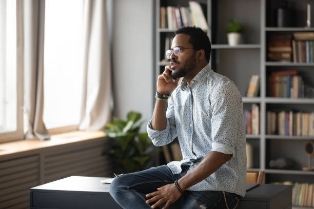 istock Serious African American man talking on phone, sitting on desk 1270850797