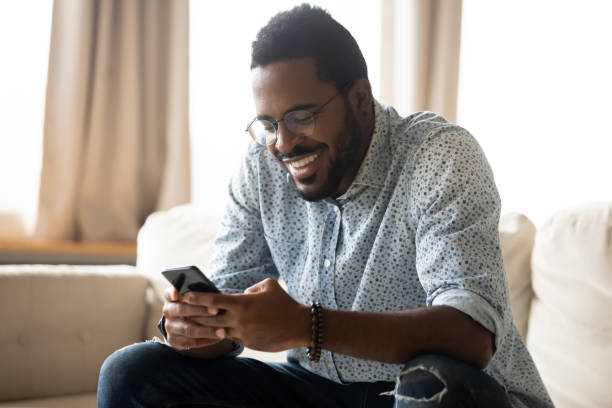 istock Smiling African American man using phone, sitting on couch 1270851165