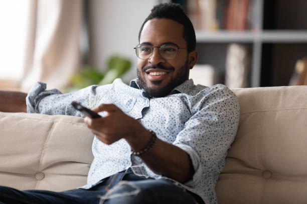 istock Smiling African American man using tv controller, sitting on couch 1270851175