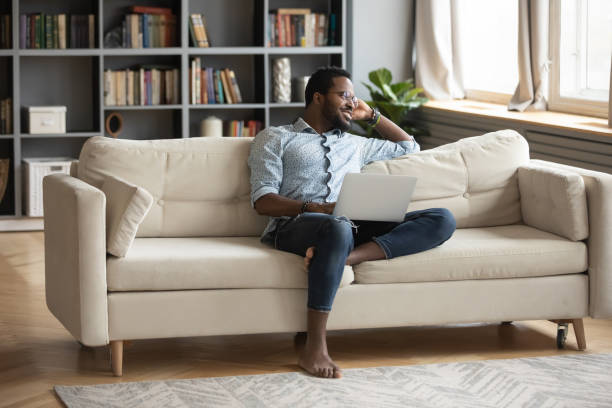 istock Thoughtful African American man relaxing on couch with laptop, visualizing 1270851180